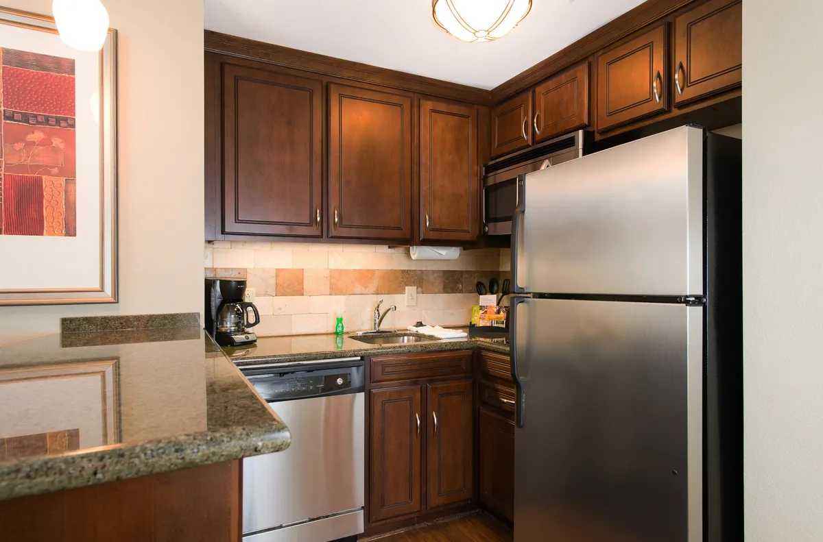 This image showcases a modern kitchen with wooden cabinets, stainless steel appliances, and a granite countertop. The visible appliances include a stove and refrigerator, suggesting a fully equipped cooking space ideal for preparing meals. The warm tones and functional layout evoke a sense of homey comfort and practicality.