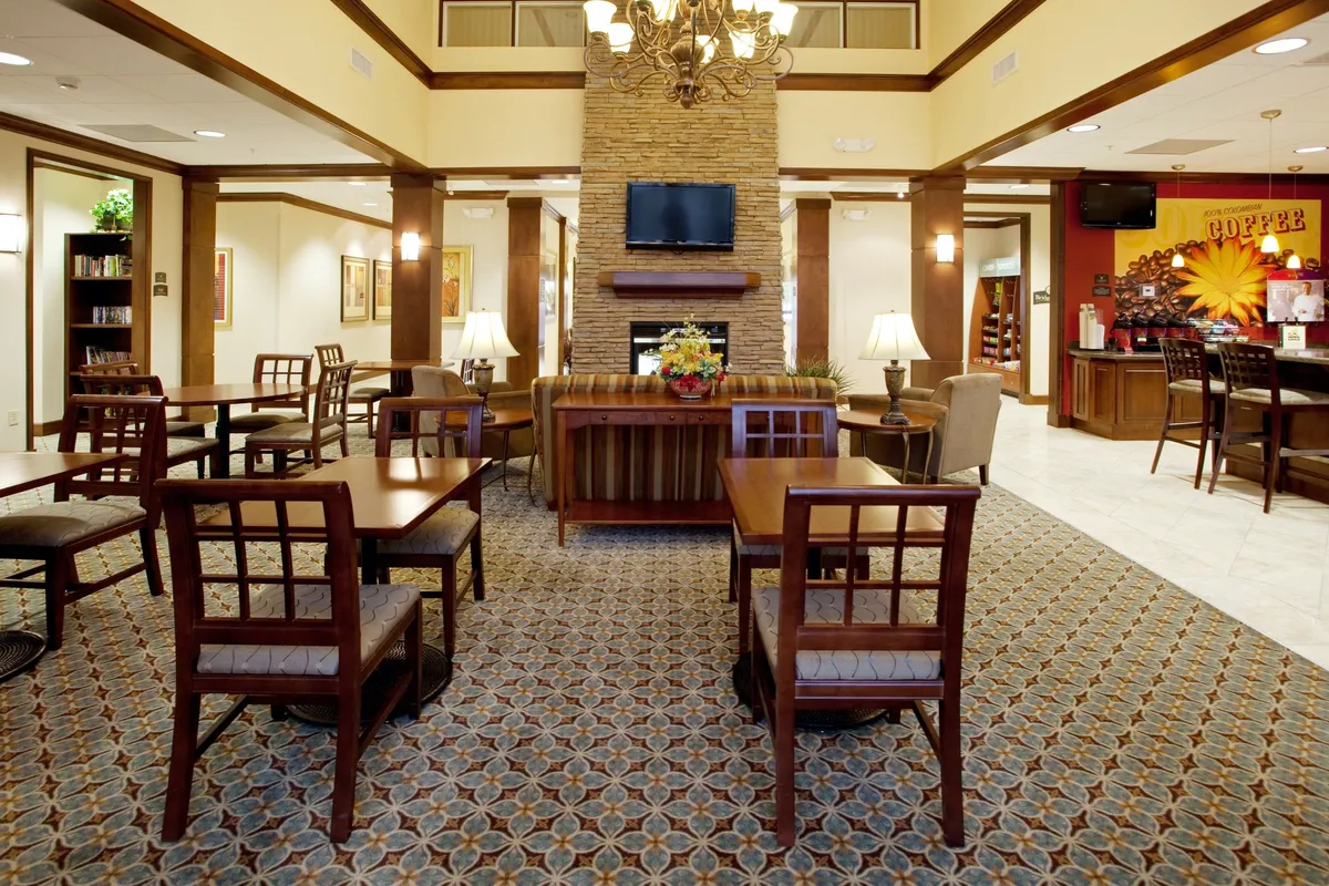 A stylish lounge with a central fireplace, elegant chandelier, and a cozy seating arrangement. Nearby, a coffee bar invites guests to relax and socialize. The scene is bathed in soft light, creating a welcoming atmosphere that encourages both relaxation and community interaction.