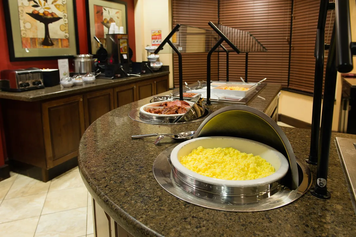 A well-stocked buffet counter with various food items and decorative artwork sets the stage for social dining. Guests are seen serving themselves, mingling, and enjoying the friendly atmosphere, echoing the communal spirit of evening receptions.