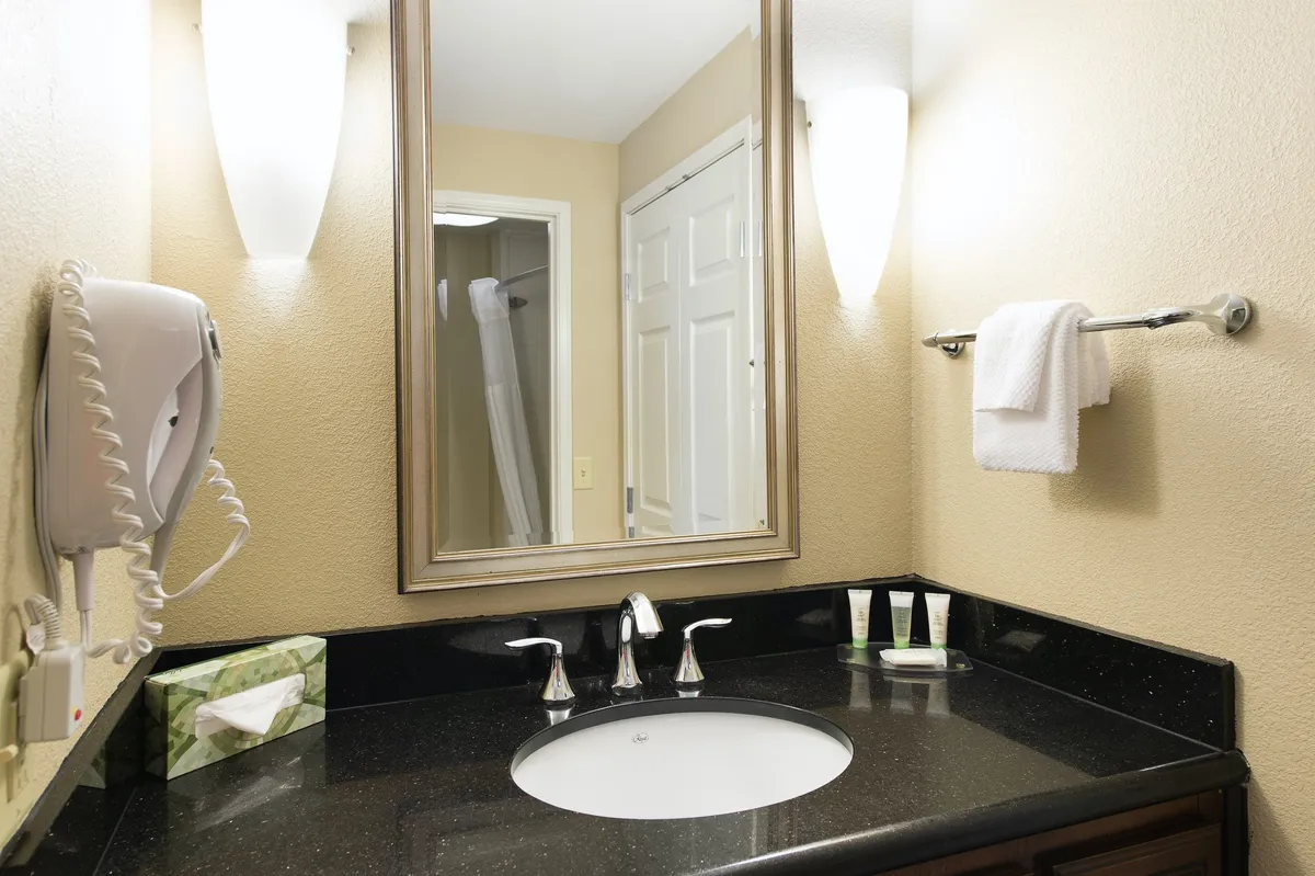 A modern bathroom featuring a sleek sink, large mirror, and bright light fixtures. The countertop is neatly organized, suggesting a clean and fresh environment ideal for grooming and self-care.