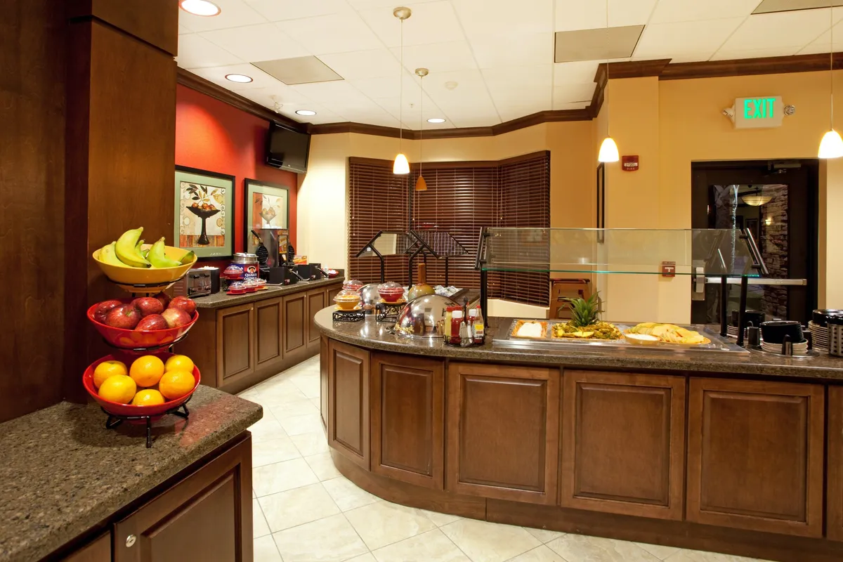 A welcoming buffet area with a colorful fruit display, bright artwork, and guests enjoying breakfast. The atmosphere is lively and social, illustrating the communal dining experience available to hotel guests.