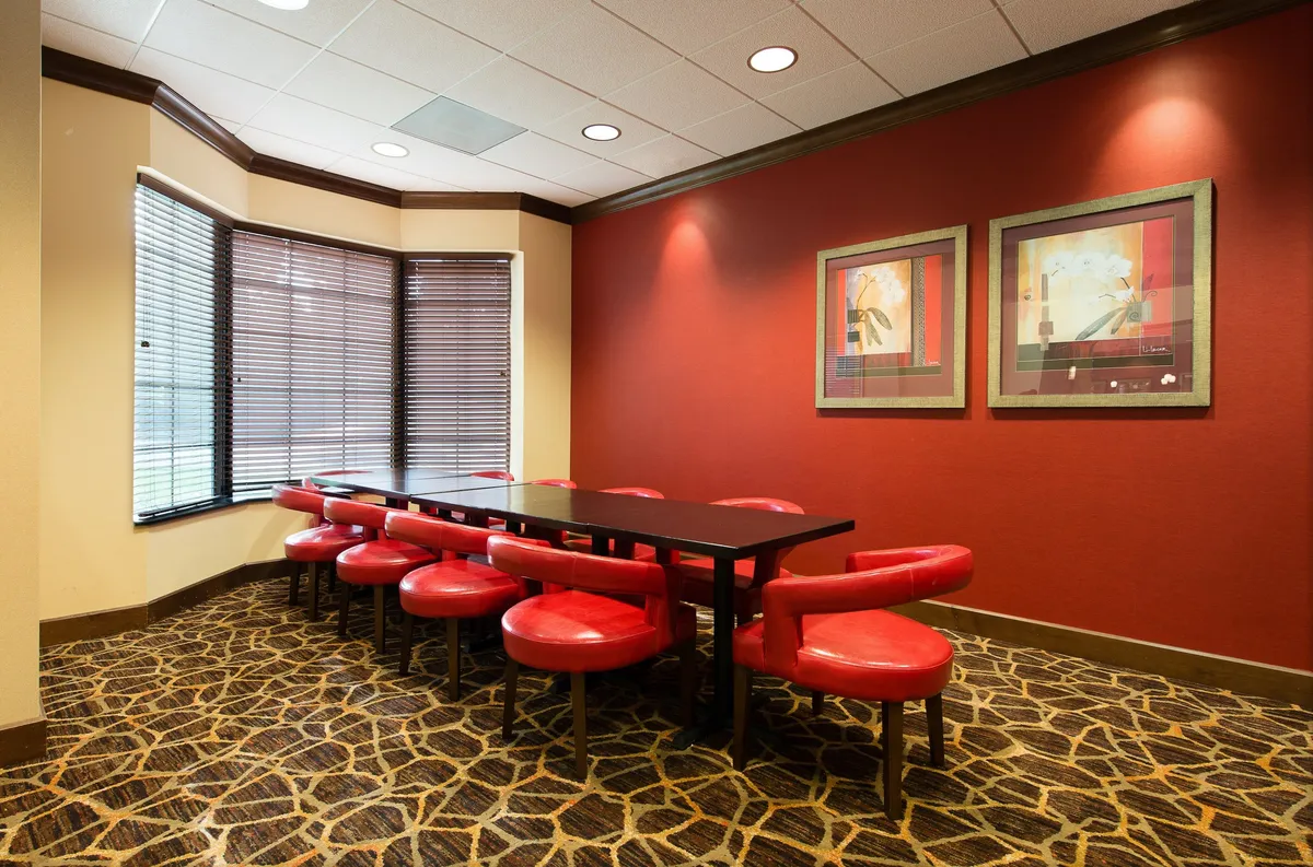 A modern workspace with a long black table surrounded by striking red circular chairs, complemented by framed artwork on the wall. The space is set up for both business meetings and informal gatherings, providing an energetic yet comfortable atmosphere for productivity.